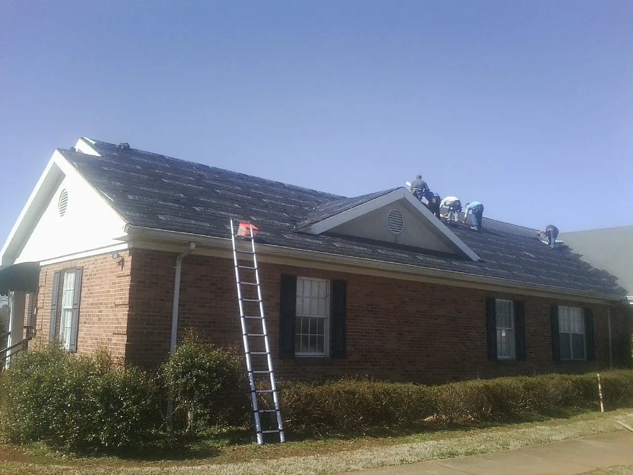 Crew tearing shingles off a brick ranch roof with a ladder set — Emergency Roof Repair work by our crew in Ashland